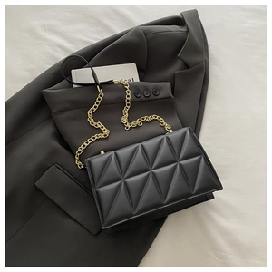 Quilted black crossbody bag with gold chain strap on grey blazer and white background