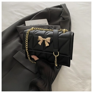 Close-up of quilted leather texture and golden bow detail on a black chain bag