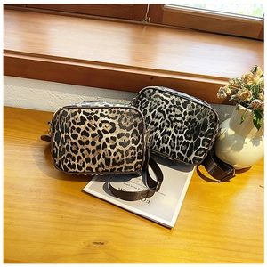 Close-up of leopard print camera bags with wide fabric straps on a rustic wooden desk