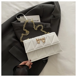 Detail of white quilted crossbody bag featuring a golden bow buckle and chain strap