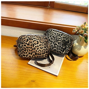 Detailed view of leopard print crossbody travel bags on a wooden surface with accessories