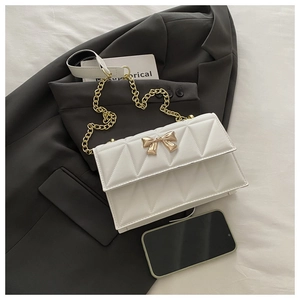 Close-up of white quilted leather bag with a golden metal bow and chain strap detail