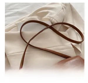 Detail of adjustable brown leather strap and silver metal buckle on a shoulder bag