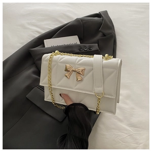 Close-up of quilted white chain bag with golden bow buckle on a stylish suit background