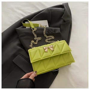 Detailed macro view of green quilted bag featuring a golden metal bow and chain strap