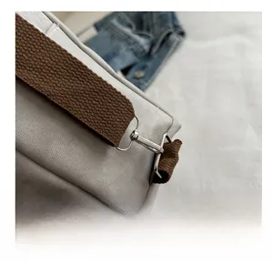 Detail of silver metal hook and brown woven strap on a gray canvas backpack