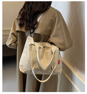 Detail of beige nylon tote bag with red Fashion tag shown on model's shoulder