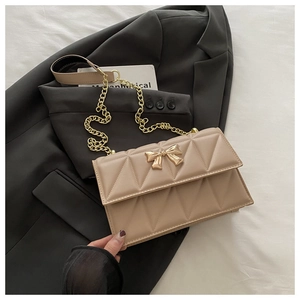 Close-up of quilted beige leather crossbody bag with golden bow buckle and chain strap
