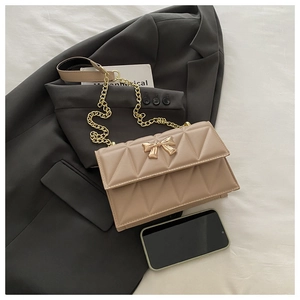 Detail showing the apricot quilted crossbody bag with a gold bow buckle and chain strap