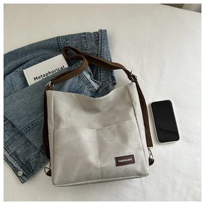 Detailed view of light gray faux leather bag with front pockets and wide fabric strap