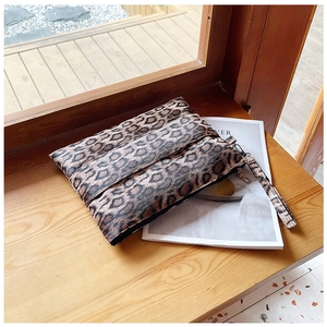 Chic leopard print clutch bag with wristlet strap resting on a wooden window sill
