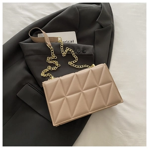Detailed view of beige quilted handbag with gold chain strap on a grey blazer