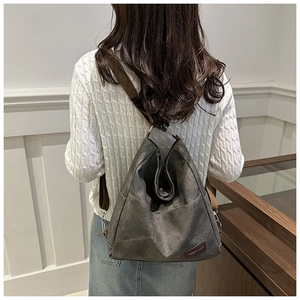 Detailed view of dark grey canvas backpack with brown straps worn by a model in a minimalist setting