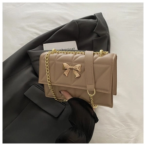 Detail shot of beige quilted handbag with gold bow ornament and chain strap