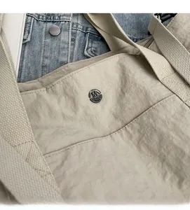 Detail of beige nylon tote bag with pleated texture and circular metal logo plaque