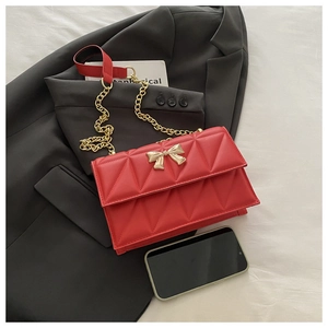 Detail of red quilted leather bag featuring a golden bow-shaped clasp and chain strap