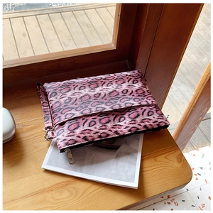 Pink leopard print clutch bag with metallic zipper on a wooden windowsill