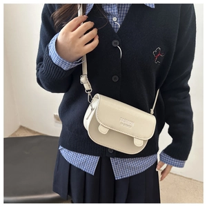 Detail of cream fashion crossbody bag featuring embossed text and silver metal hardware