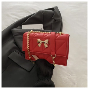Close-up of red quilted handbag featuring a golden metal bow buckle and chain strap