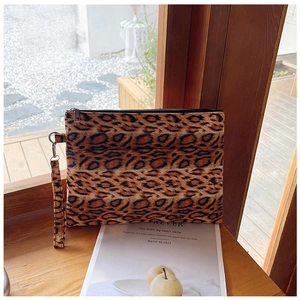 Close-up of leopard print clutch bag with wristlet strap and zipper on a wooden ledge