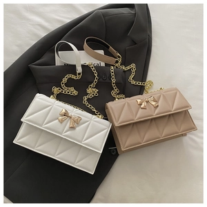 Close-up of quilted chain crossbody bag with golden bow clasp on a dark blazer