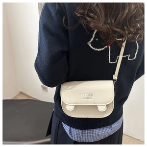 Detail view of cream crossbody bag with letter embossing worn by model on navy sweater