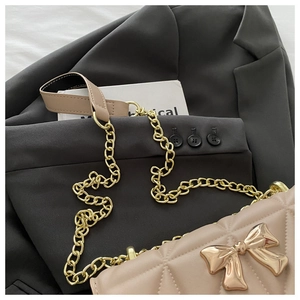 Close-up of quilted chain bag with large golden bow buckle and fine metal strap