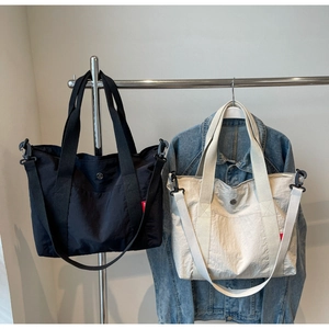 Detail of large nylon tote bags in black and beige with side labels hanging on rack