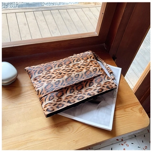 Close-up of leopard print clutch bag with silver zipper and wrist strap on a wooden desk