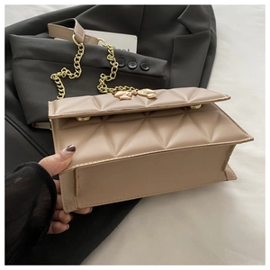 Detail of cream quilted crossbody bag with golden bow clasp and chain strap