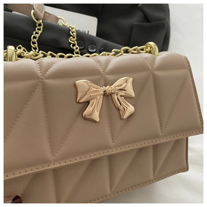 Detailed close-up of quilted leather bag with metallic bow and chain strap details