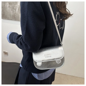 Silver metallic crossbody square bag with embossed text shown on a navy blue knit sweater