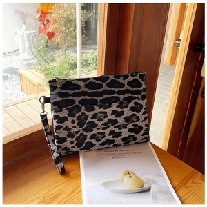 Detailed view of leopard print clutch bag with leather texture and wristlet on wooden ledge
