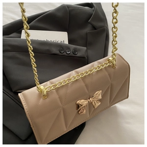 Detail of beige quilted bag with gold bow clasp and metallic chain strap on gray blazer