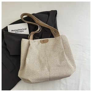 Dettaglio borsa tote in paglia intrecciata con manici in pelle marrone su sfondo bianco