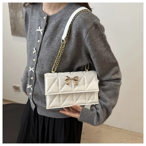 Detail of white quilted crossbody bag featuring a golden bow accent and chain strap
