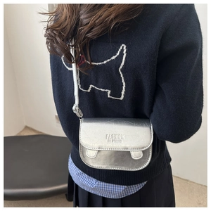 Detail of metallic silver crossbody bag with textured faux leather and flap closure