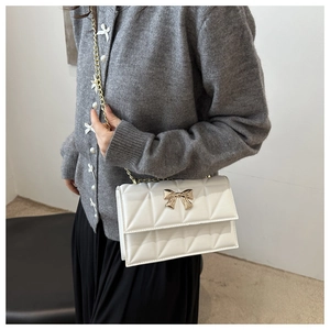 Detail of white quilted bag featuring a gold bow-shaped lock and luxury metal chain strap