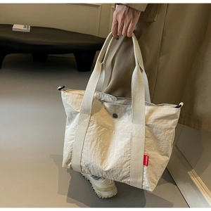 Detail of off-white nylon tote bag with wide strap handles and red fashion label