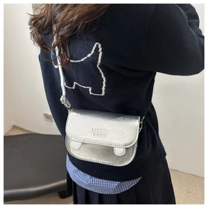 Detail of silver metallic crossbody bag with ruffled design and embossed fashion text