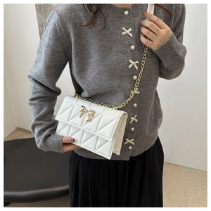 Detail of quilted creamy white crossbody bag with golden bow clasp and chain strap