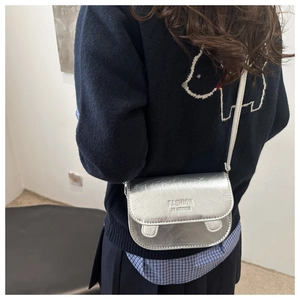 Detail of silver crossbody bag with FASHION IN STINCE embossing and metallic PU texture