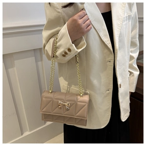 Chic beige quilted crossbody bag featuring a golden bow accent and metal chain strap