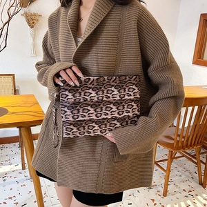Fashionable leopard print clutch bag with wrist strap held by a model in a warm setting