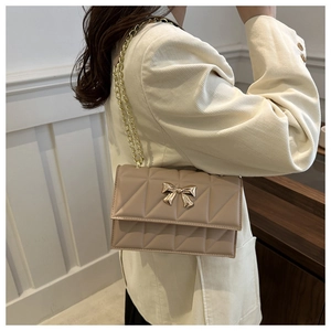 Close-up of beige quilted crossbody bag with gold bow clasp and metallic chain strap