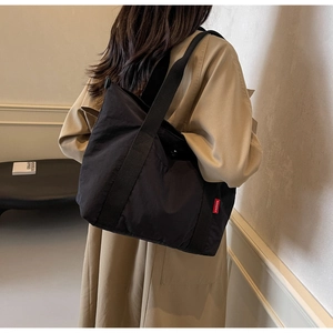 Detailed view of black nylon tote bag with red Fashion label on a model in beige trench coat