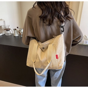Detail of beige nylon tote bag with removable strap and FASHION label on model