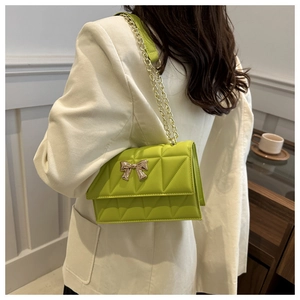Detailed view of neon green quilted crossbody bag with gold bow lock on white blazer