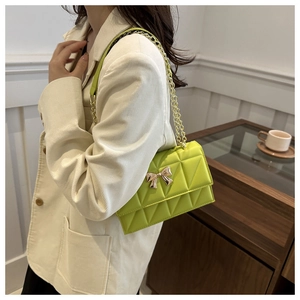 Close-up of lime green quilted chain bag with a gold bow buckle on a beige suit