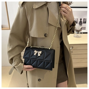 Detail shot of a black quilted shoulder bag with golden bow clasp on a trench coat